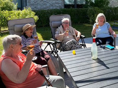 Vier Seniorinnen sitzen im Garten und genießen bei Sonnenschein gemeinsam Getränke.
